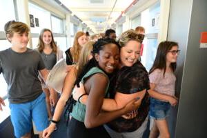 A Fieldston Middle student and a teacher smile and hug on the first day of school as other students walk past them in a hallway
