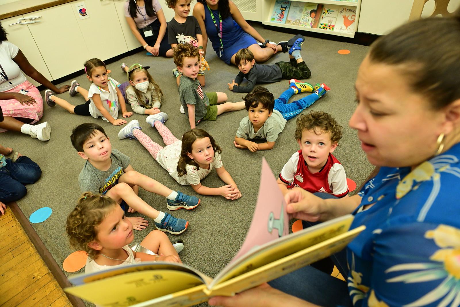 Ethical Culture's youngest learners listen on carpet as teacher reads from a book.